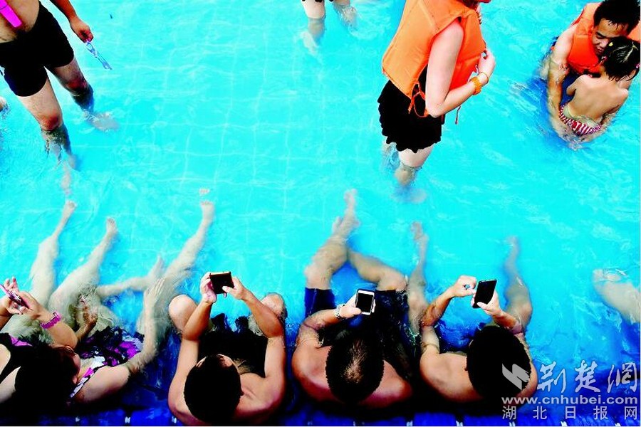 人在碧波中蕩漾,本為求一身清涼,但對于低頭族來說,此時此刻仍不能離開自己的手機。于是炎炎夏日里,在游泳館、親水樂園、東湖里、長江上……一邊玩著水,一邊刷手機的人,成了一道特別的風景。當然,他們給手機也穿上了“泳衣”——透明的防水手機套。這樣,就算手是濕的,就算身邊有波浪,甚至就算在水下,手機也與自己形影不離。圖為:擁擠的游泳池里一角,許多嬉水者在忘情地玩著手機