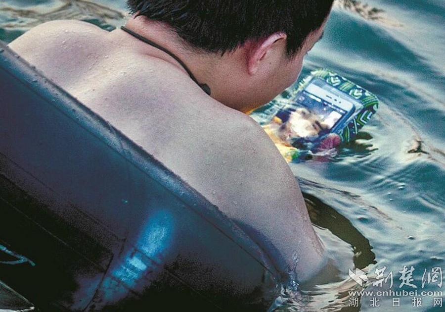 2017中國互聯網絡發展狀況統計報告顯示,截至2017年6月,我國網民規模達到7.51億,手機網民規模達7.24億。可能是手機太過于深入人們的生活,就算難得有點休閑時間,大家仍會下意識地握緊手機。在手機最不易“生存”的水上,人們也不愿動搖這個習慣。明明是與朋友相聚在水上樂園,仍是一人抱一部手機,很少互相對個眼神;明明是親子游泳,家長只顧自己埋頭看手機,根本沒注意孩子的一臉無奈。 圖為:與手機一同“潛”行